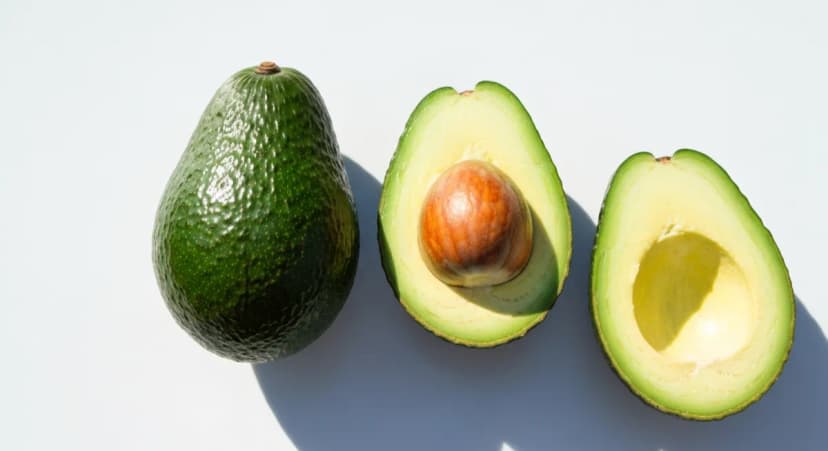 Three avocados. Whole, halved showing pit, and empty half. On white surface